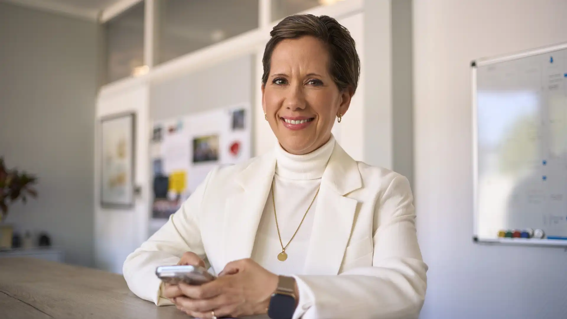 Eine Frau sitzt an einem Tisch und hält ein Mobilgerät in der Hand.