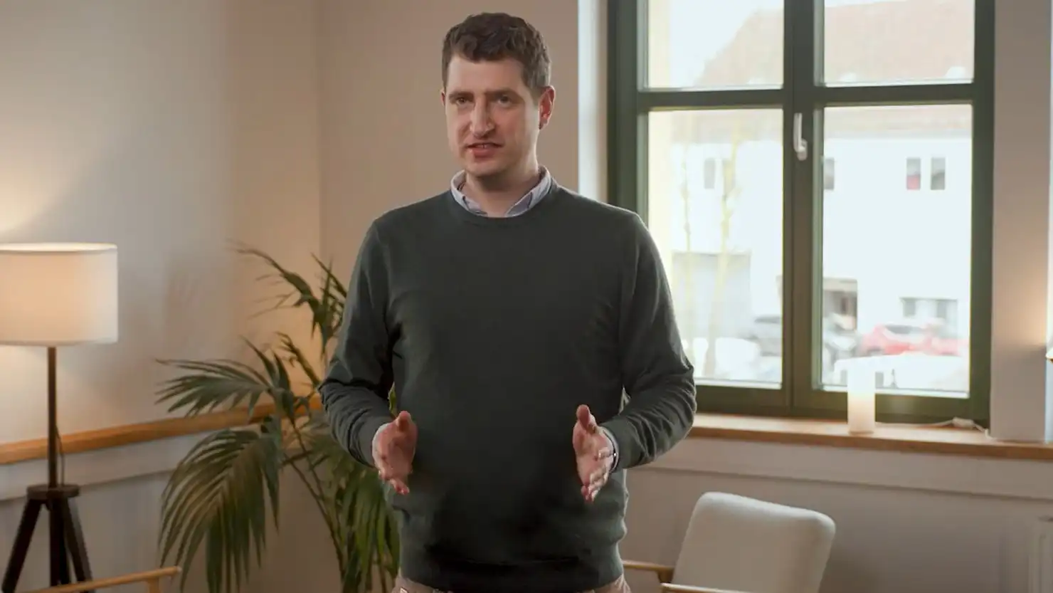 Ein Mann steht in einem Raum vor einer Sitzecke und spricht zu Steuerthemen